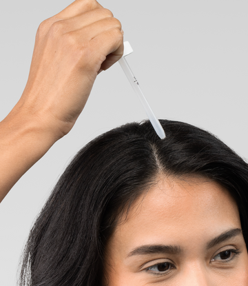 スポイトで髪の分け目に沿って液体ヘアトリートメントを塗る女性。