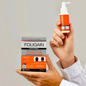 FOLIGAIN男性用TRIOXIDIL 10%外用トリートメントの箱とスプレーボトルを持つ両手。