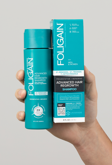 箱の横で、青緑色のボトルに入ったFOLIGAINアドバンストヘアリグロースシャンプーを持つ手。