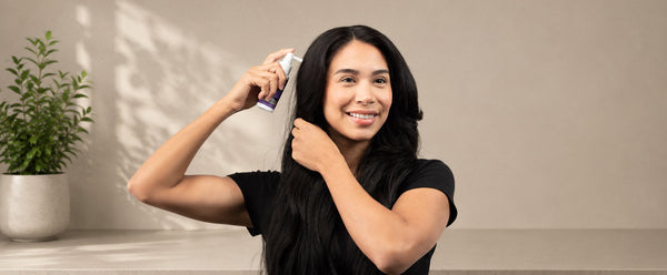髪を分け、頭皮の近くにFOLIGAIN TRIOXIDILのスプレーアプリケーターを持つ女性。